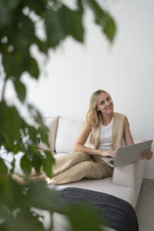 Lächelnder Freiberufler mit Laptop auf dem Sofa zu Hause - SVKF01103