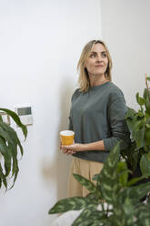 Lächelnde Frau mit Kaffeetasse an der Hauswand stehend - SVKF01158