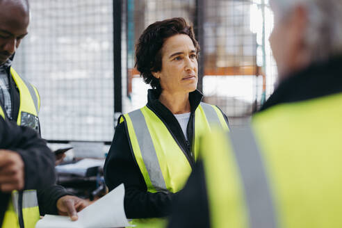 Eine weibliche Lagerverwalterin bei einer Personalbesprechung mit ihren Kollegen in einem Vertriebszentrum. Eine Gruppe verschiedener Mitarbeiter arbeitet in einem Logistikzentrum zusammen. - JLPSF29009