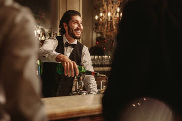 Barkeeper, der einem Gast an der Bar ein Getränk serviert. Nachtclub-Barkeeper, der Whiskey in ein Glas gießt, während ein Mann an der Theke steht. - JLPSF29023