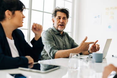 Älterer Mann im Gespräch mit seinem Team während einer Besprechung in einem Büro. Älterer Geschäftsmann in einer Diskussion mit seinen Kollegen. Geschäftsleute in einem Sitzungssaal. - JLPSF29055