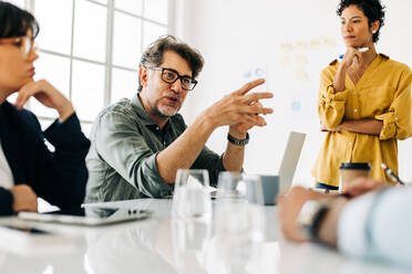 Ein Geschäftsmann erklärt seinem Team ein Projekt. Ein älterer Geschäftsmann übernimmt während einer Besprechung die Führung. Eine Gruppe von Geschäftsleuten diskutiert über die Arbeit in einem Büro. - JLPSF29056