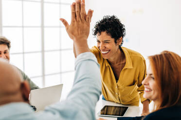 Colleagues doing a high five in an office. Successful business people celebrating a goal achievement. Happy business professionals having a meeting in a boardroom. - JLPSF29061