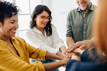 Diverse business team stacking hands together in a huddle. Group of happy business people having a meeting in an office. Team unity in the workplace. - JLPSF29097