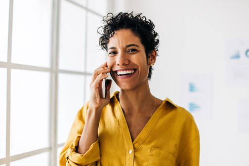 Eine Frau telefoniert mit einem ihrer Geschäftspartner in einem Büro. Eine Geschäftsfrau lächelt, als sie mit einem Mobiltelefon über ein Geschäft spricht. Verbindungen herstellen, die zum Erfolg führen. - JLPSF29100