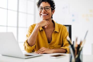 Schwarze Geschäftsfrau, die an ihrem Schreibtisch in einem Büro arbeitet. Die Geschäftsfrau lächelt in die Kamera, sie genießt ihre Arbeit als Technikerin. - JLPSF29113