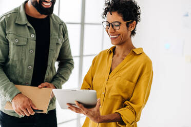 Geschäftsfrau, die mit ihrem Kollegen ein Tablet benutzt, während sie in einem Büro steht. Glückliche Geschäftsleute, die ein neues Projekt besprechen. Teamwork und Zusammenarbeit in einem Startup. - JLPSF29121