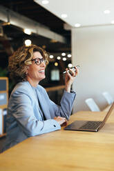 Happy business woman having a phone call conversation in an office. Professional woman speaking with her associates on a mobile phone. Woman sitting with a laptop in a coworking office. - JLPSF29129