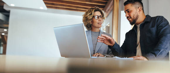 Business man having a discussion with his colleague in an office. Two business people using a laptop in a meeting. Teamwork and collaboration between business professionals. - JLPSF29148