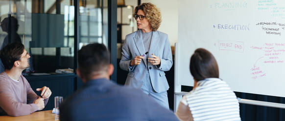 Project manager having a discussion with her team in a meeting. Business woman giving a presentation in an office boardroom. Team of professionals working together on a project. - JLPSF29167