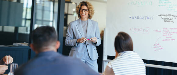 Eine Geschäftsfrau steht vor ihrem Team und bespricht ihre Ideen. Ein Geschäftsteam trifft sich in einem Sitzungssaal. Kreative Geschäftsleute arbeiten gemeinsam an einem Projekt. - JLPSF29169