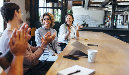 Glückliche Geschäftsleute, die während einer Besprechung in einem Büro applaudieren. Geschäftskollegen, die in einem Sitzungssaal ihren Erfolg feiern. Ein Team von Fachleuten, die in einem Startup zusammenarbeiten. - JLPSF29199
