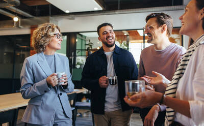 Zufriedene Kollegen bei einer Kaffeepause in einem Büro. Eine Gruppe von Geschäftsleuten unterhält sich an einem Arbeitsplatz. Geschäftsleute arbeiten in einem Startup. - JLPSF29201