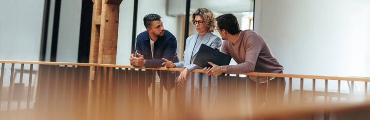 Diskussion in einem Büro. Drei Geschäftsleute unterhalten sich auf einem Innenraumbalkon. Eine Gruppe von Innenarchitekten arbeitet gemeinsam an einem Projekt, sie sind in einem neu gegründeten Unternehmen tätig. - JLPSF29219