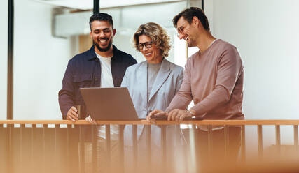 Happy business people video calling their associates on a laptop. Group of design professionals standing together and having an online meeting. Creative business team working in a startup. - JLPSF29222