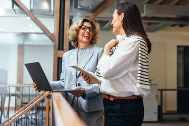 Lächelnde Geschäftsfrauen bei einer Besprechung auf einem Balkon. Professionelle Geschäftsfrauen besprechen ihre anstehende Arbeit und wie sie diese erledigen können. Frauen arbeiten in einem von Frauen geführten Start-up zusammen. - JLPSF29228