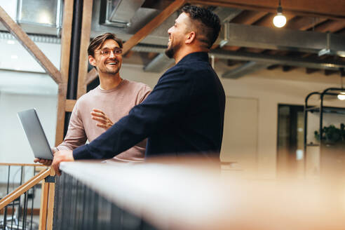 Männliche Techniker diskutieren in einem Büro. Zwei Geschäftsleute sprechen über ein Projekt, während sie auf einem Innenbalkon stehen. - JLPSF29231