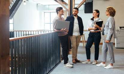 Tech professionals having a standup meeting in an office. Business people stand together and discuss their work progress in an office. Creative business team working together in a startup. - JLPSF29234