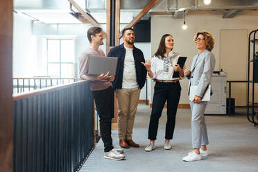 Professionals having a team meeting in an office. Group of business people standing together and discussing their work and projects. Business team doing a standup in the morning. - JLPSF29237