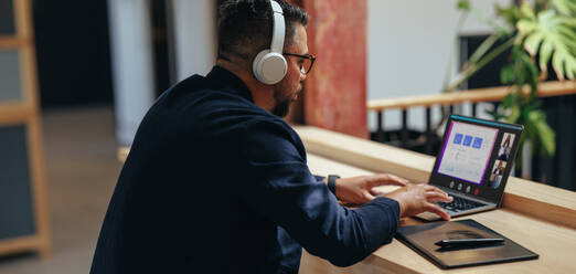 Männlicher Designer, der eine Videokonferenz mit seinem Team in einem Coworking-Büro abhält. Professioneller Mann, der in einem Online-Meeting Finanzdaten diskutiert. Geschäftsmann, der mit einem Laptop ferngesteuert arbeitet. - JLPSF29256