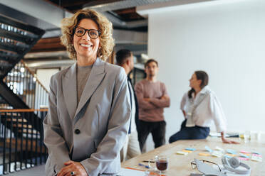 Mature woman in her 40's having a meeting with her team. Happy business woman looking at the camera in a boardroom. Female professional working on a with her colleagues in a creative startup. - JLPSF29277
