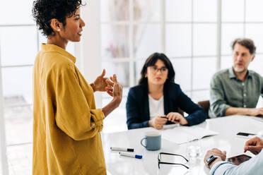 Eine weibliche Teamleiterin hält eine Rede in einem Sitzungssaal. Eine schwarze Geschäftsfrau bespricht ein Projekt mit ihren Kollegen in einem Büro. Eine Gruppe von Geschäftsleuten hat eine Besprechung. - JLPSF29285
