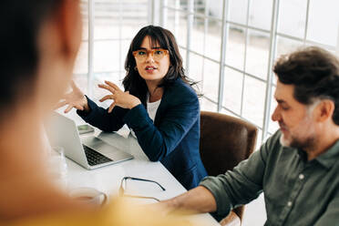 Eine Geschäftsfrau diskutiert mit ihrem Team in einer Besprechung. Eine junge Geschäftsfrau spricht mit ihren Kollegen in einem Sitzungssaal. Eine Gruppe von Geschäftsleuten arbeitet in einem Büro zusammen. - JLPSF29292