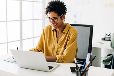 Grafikdesignerin lächelt, während sie in einem Büro an einem Laptop arbeitet. Frau benutzt ein Grafiktablett, um Zeichnungen anzufertigen. Kreative Geschäftsfrau genießt die Arbeit an ihrem Projekt in einem Büro. - JLPSF29322