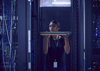 Female technician holding hard drive in server room - TETF01884