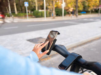 Von oben der Ernte anonyme Frau in blauen Pullover Reiten Elektrofahrrad während SMS-Nachricht über Handy im Park auf Herbst Tag - ADSF42741