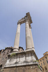 From below damaged columns of Temple of Apollo Sosianus against cloudless blue sky on street of Rome, Italy - ADSF42772