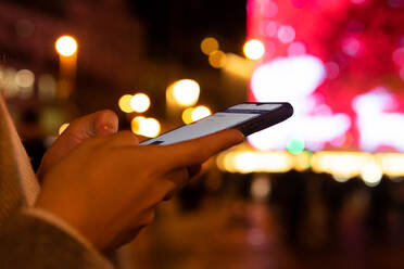 Seitenansicht einer abgeschnittenen, nicht erkennbaren Frau, die mit ihrem Handy telefoniert, während sie nachts auf einer Straße steht - ADSF42803