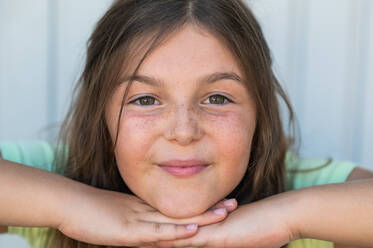 Positive brown haired girl with green eyes and freckles looking at camera while putting chin on hands - ADSF42826