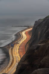 From above long exposure drone view of Miraflores boardwalk and asphalt road with bright trails of light located on coast of sea in evening in Lima, Peru - ADSF42841