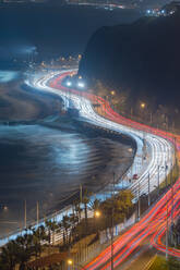 From above long exposure drone view of Miraflores boardwalk and asphalt road with bright trails of light located on coast of sea at night in Lima, Peru - ADSF42842