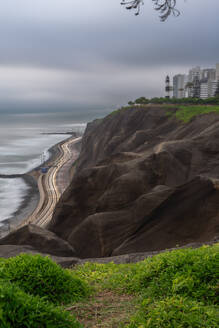 Schuss von Miraflores Promenade und kurvige Straße mit Spuren von Licht in der Nähe von Klippe mit Leuchtturm und Wohngebäuden am Ufer des Meeres in bewölkten Abend in Lima, Peru gelegen - ADSF42843