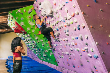 Trainerin unterstützt Kletterer an der Wand beim Bouldertraining in einer Turnhalle am Tag - ADSF42849