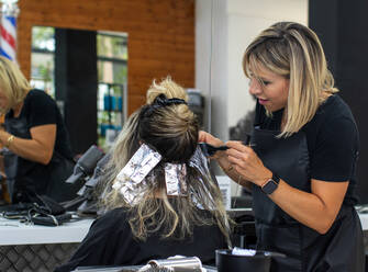 Happy blond hairstylist using brush to smear dye on woman hair - ADSF42862