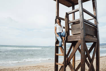 Woman sitting on lifeguard hut at beach - JOSEF16165