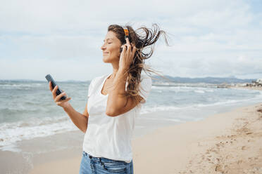 Lächelnde Frau genießt es, am Strand über Kopfhörer Musik zu hören - JOSEF16168
