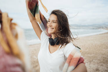 Smiling woman with hand raised at beach - JOSEF16214