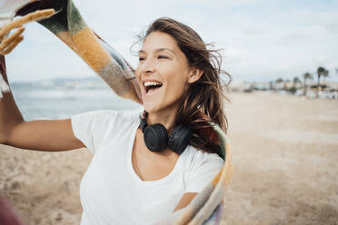 Cheerful woman with headphones enjoying at beach - JOSEF16215