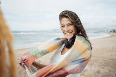 Happy woman with scarf and headphones enjoying at beach - JOSEF16216