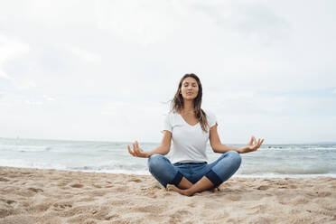 Woman practicing lotus position sitting cross-legged on sand at beach - JOSEF16230
