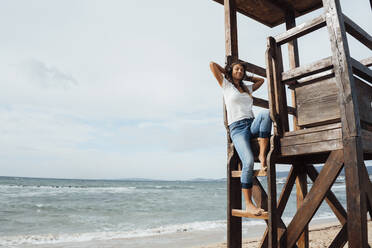Relaxed woman sitting on lifeguard hut at beach - JOSEF16236