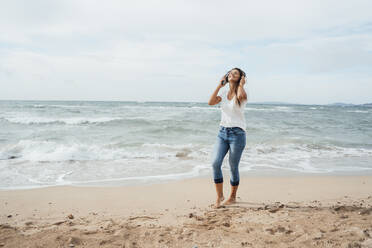 Woman enjoying listening to music at beach - JOSEF16239