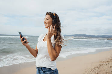 Frau genießt es, am Strand mit Smartphone und Kopfhörern Musik zu hören - JOSEF16240