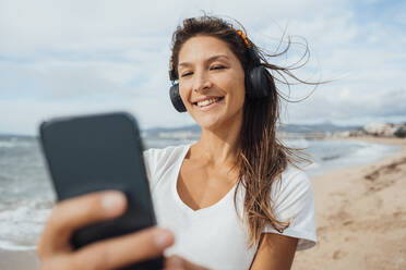 Frau mit Kopfhörern nimmt Selfie durch Smartphone am Strand - JOSEF16241