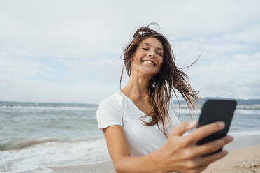 Glückliche Frau, die am Strand mit ihrem Smartphone im Internet surft - JOSEF16244