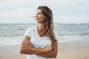 Contemplative woman standing with arms crossed at beach - JOSEF16247